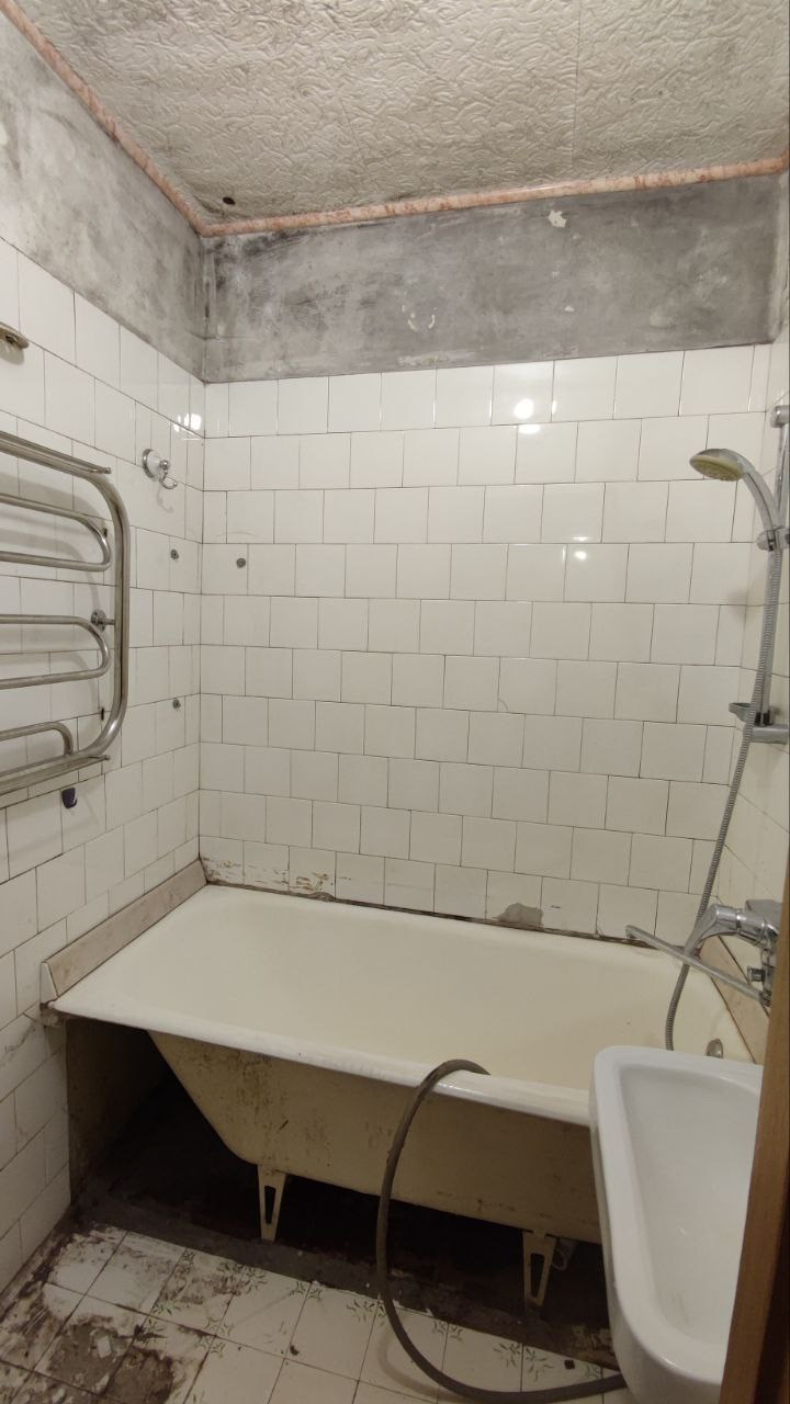 На фото старая ванная комната в хрущёвской квартире. Белая плитка в ванной на стенах. Чугунная ванна 140*70.