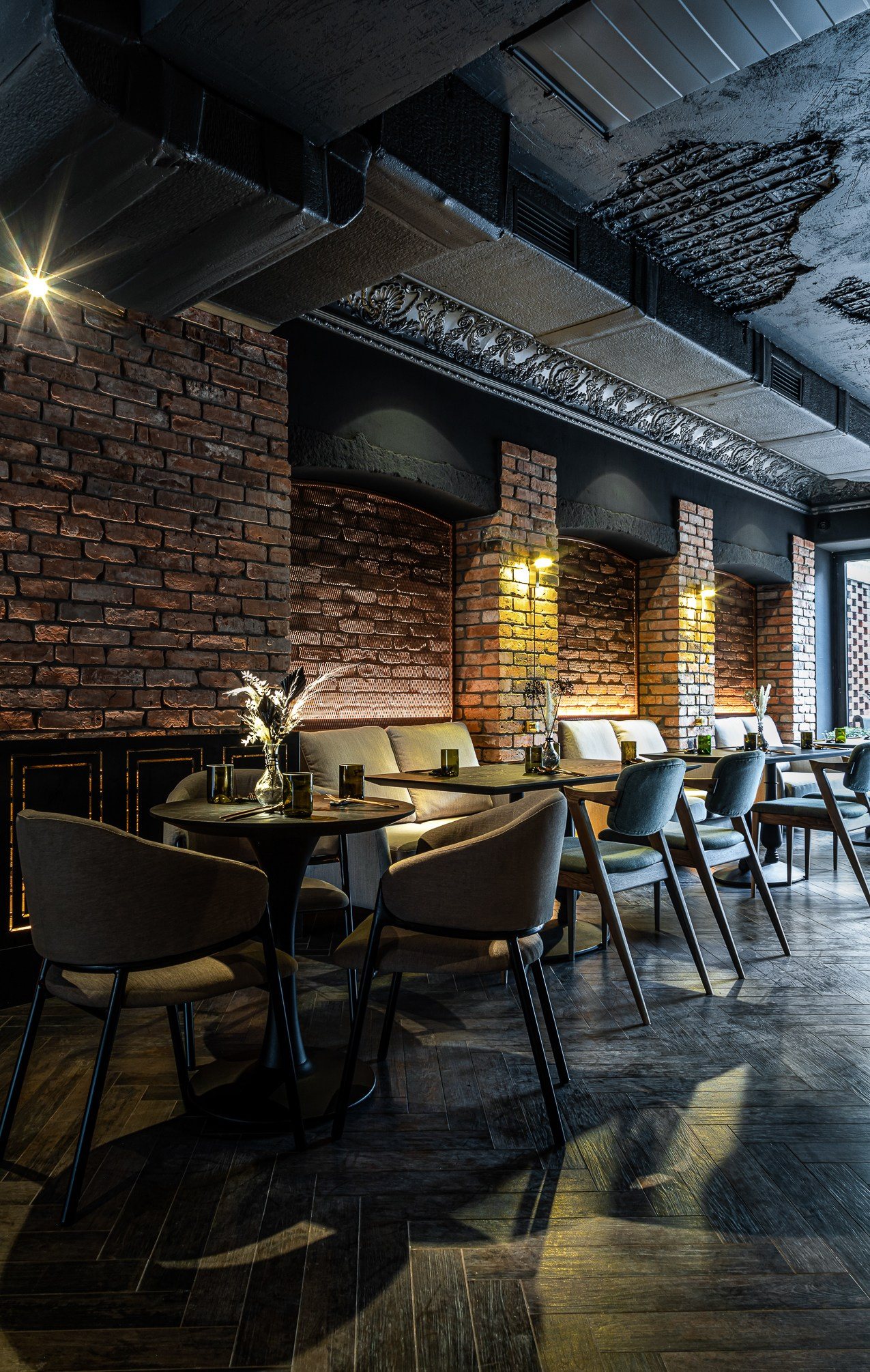 Темный зал ресторана с мебелью в центре и крашеным потолком.