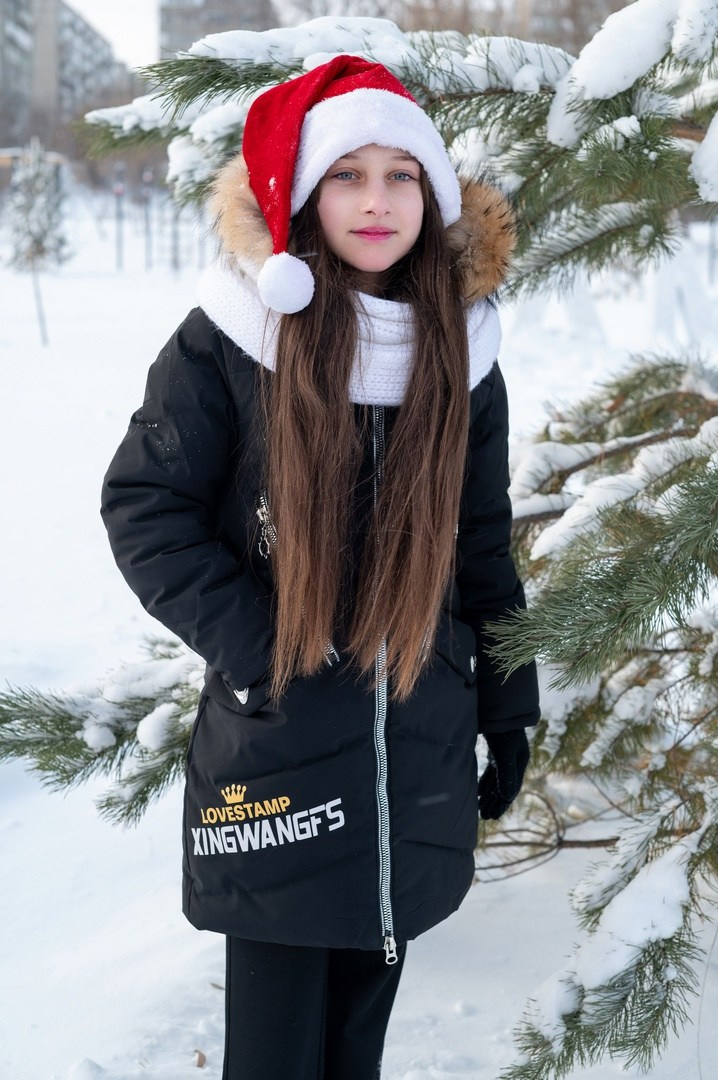 Симпатичная девочка в шапке "Деда Мороза" позирует на камеру.