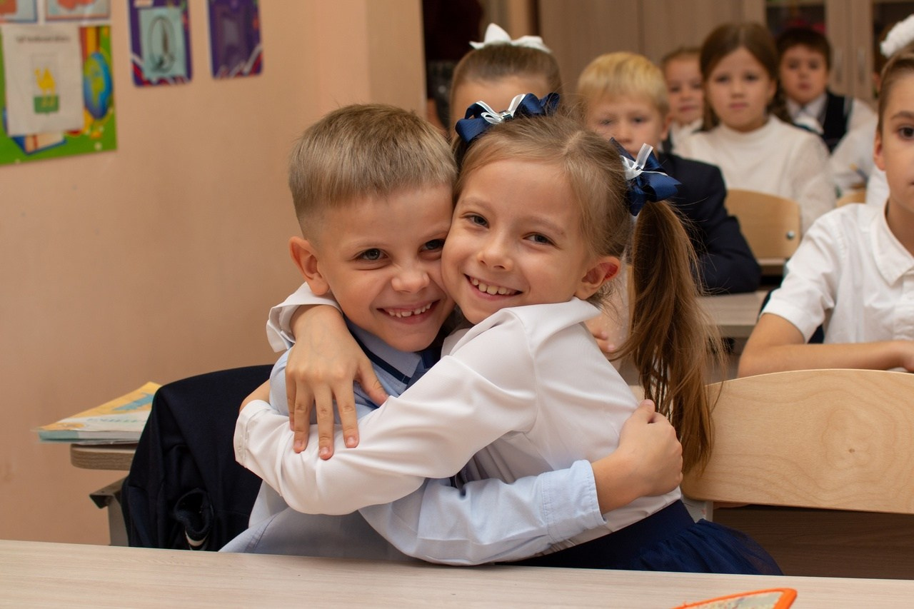 Мальчик с девочкой - первоклашки обнимаются позирую фотографу.