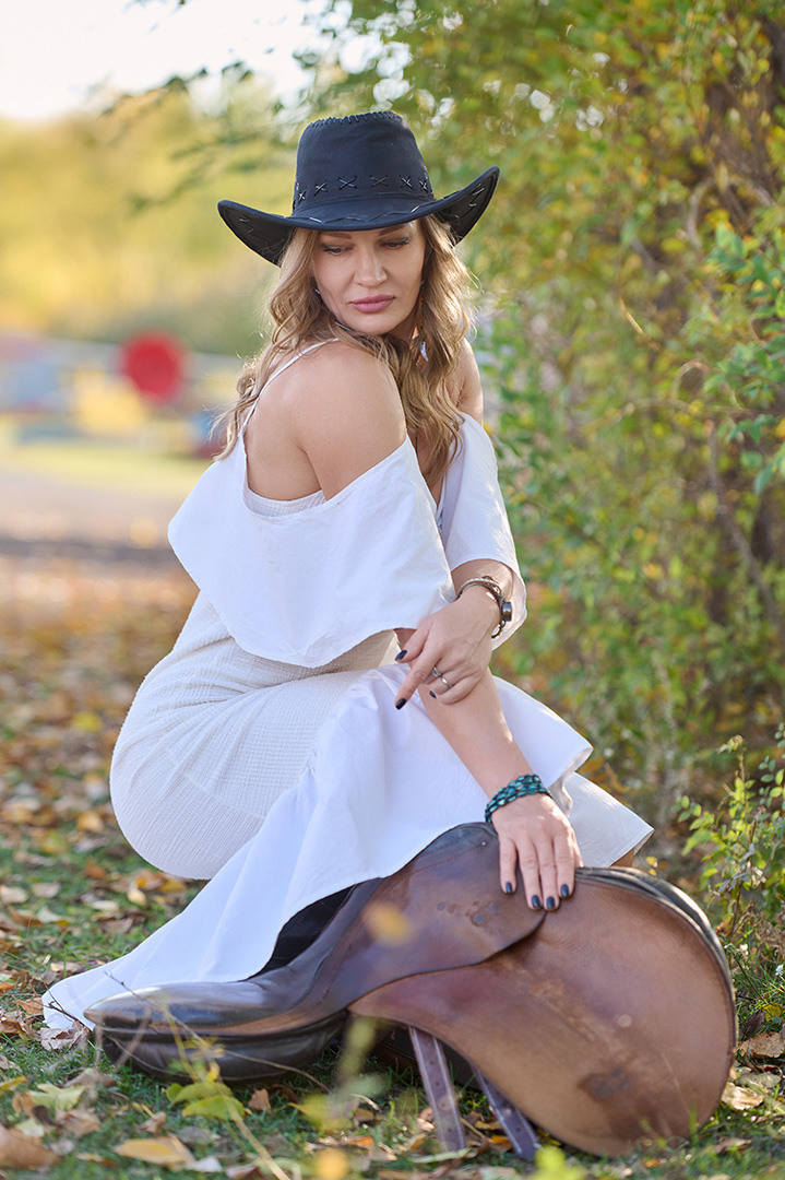 Женщина в шляпе и платье с седлом на ипподроме.