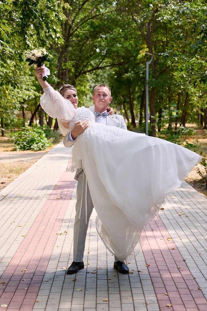 молодой муж носит на руках свою молодую жену в свадебном платье