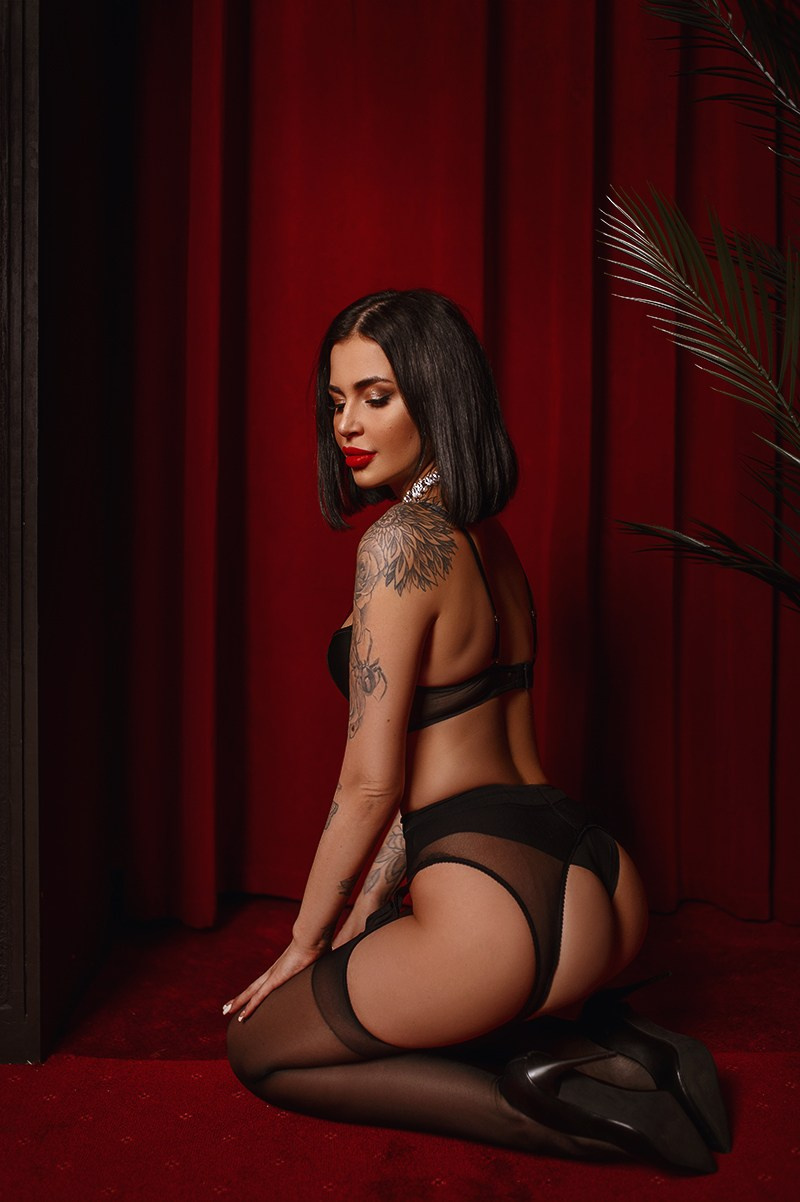 Дама в чёрном белье на коленях на красном фоне в будуарной съёмке