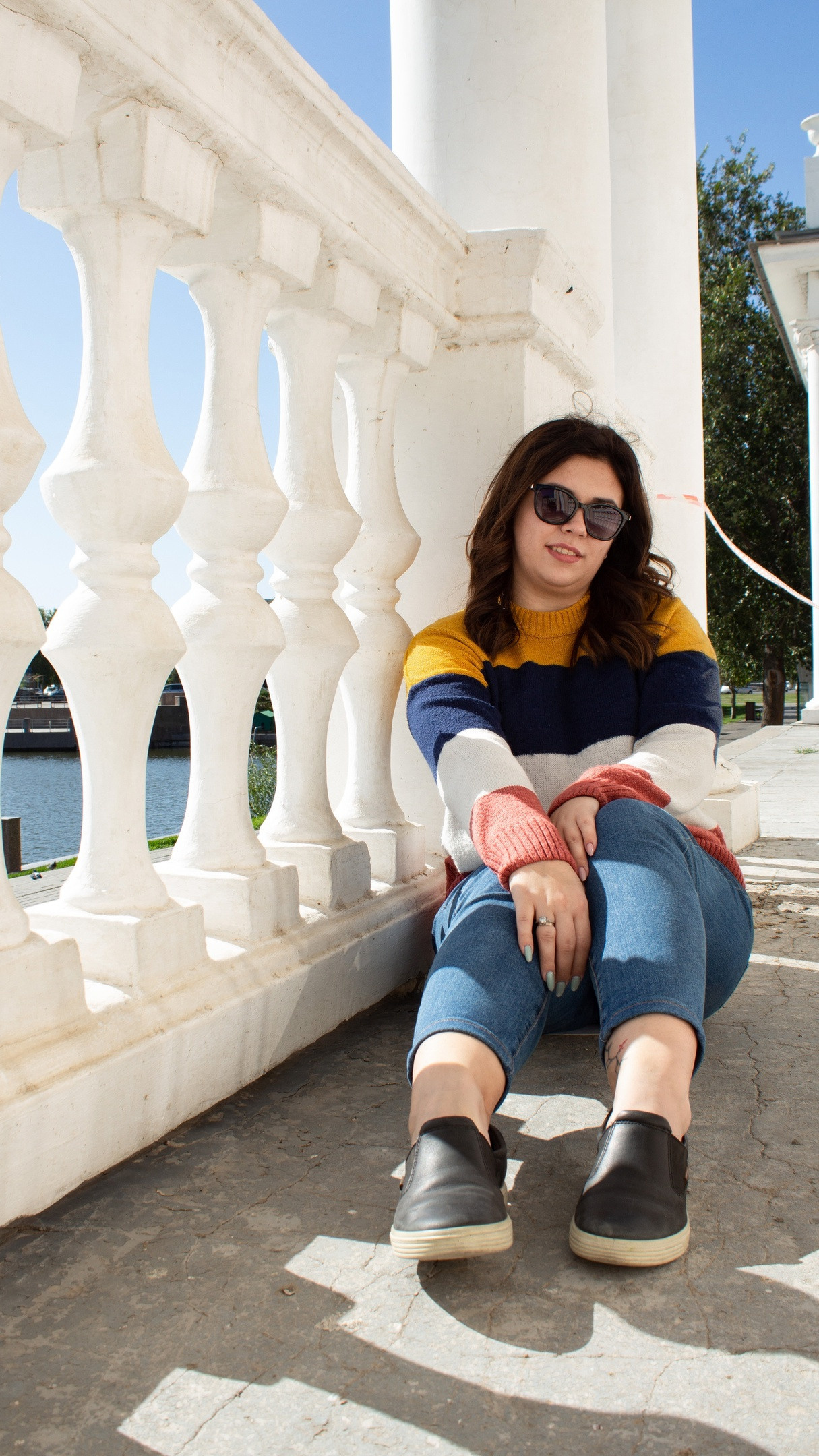 Девушка сидит на асфальте возле белого каменного ограждения. Прогулочная съёмка.