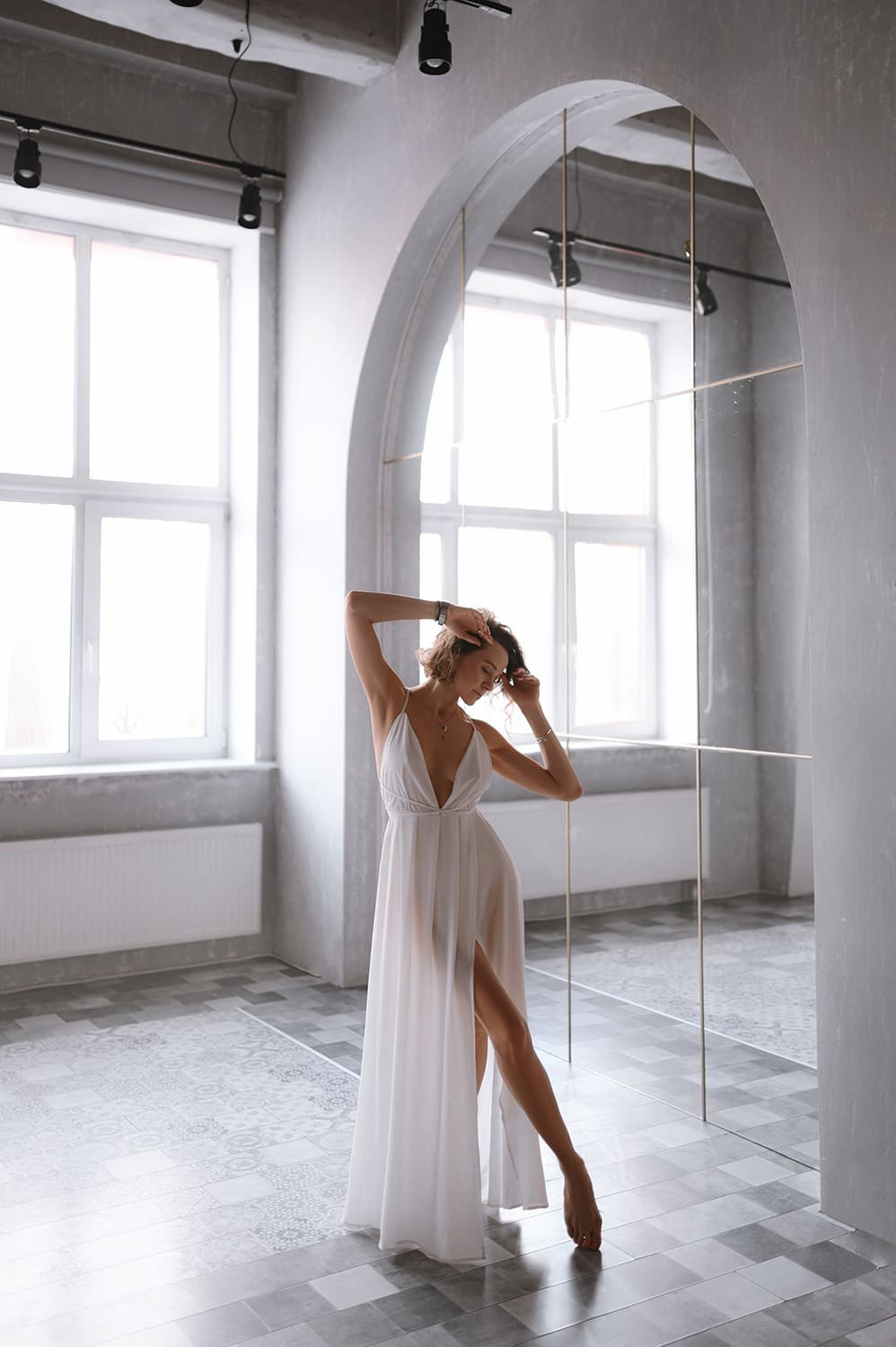 Леди в белом платье тянется в арочном помещении