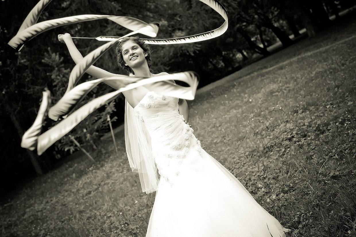 красивая невеста в белом платье развивает гимнастическую ленту в парке