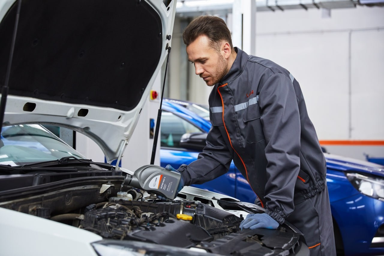 Мужчина автомеханик заливает масло в мотор автомобиля