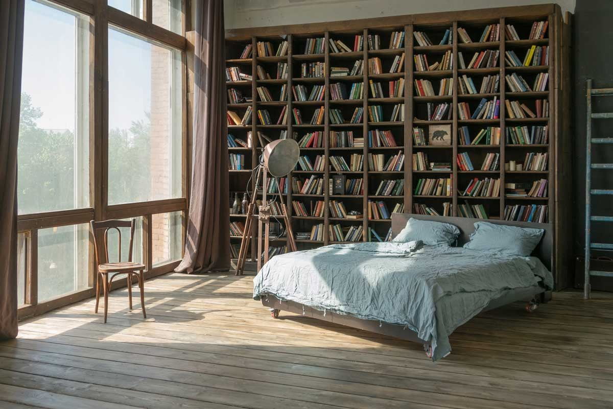 двуспальная кровать у большого окна рядом с книжным стеллажом до потолка, шторы блэкаут