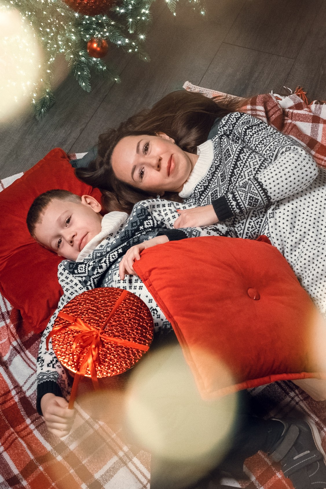 мама с сыном лежат на подушках у елки с огоньками