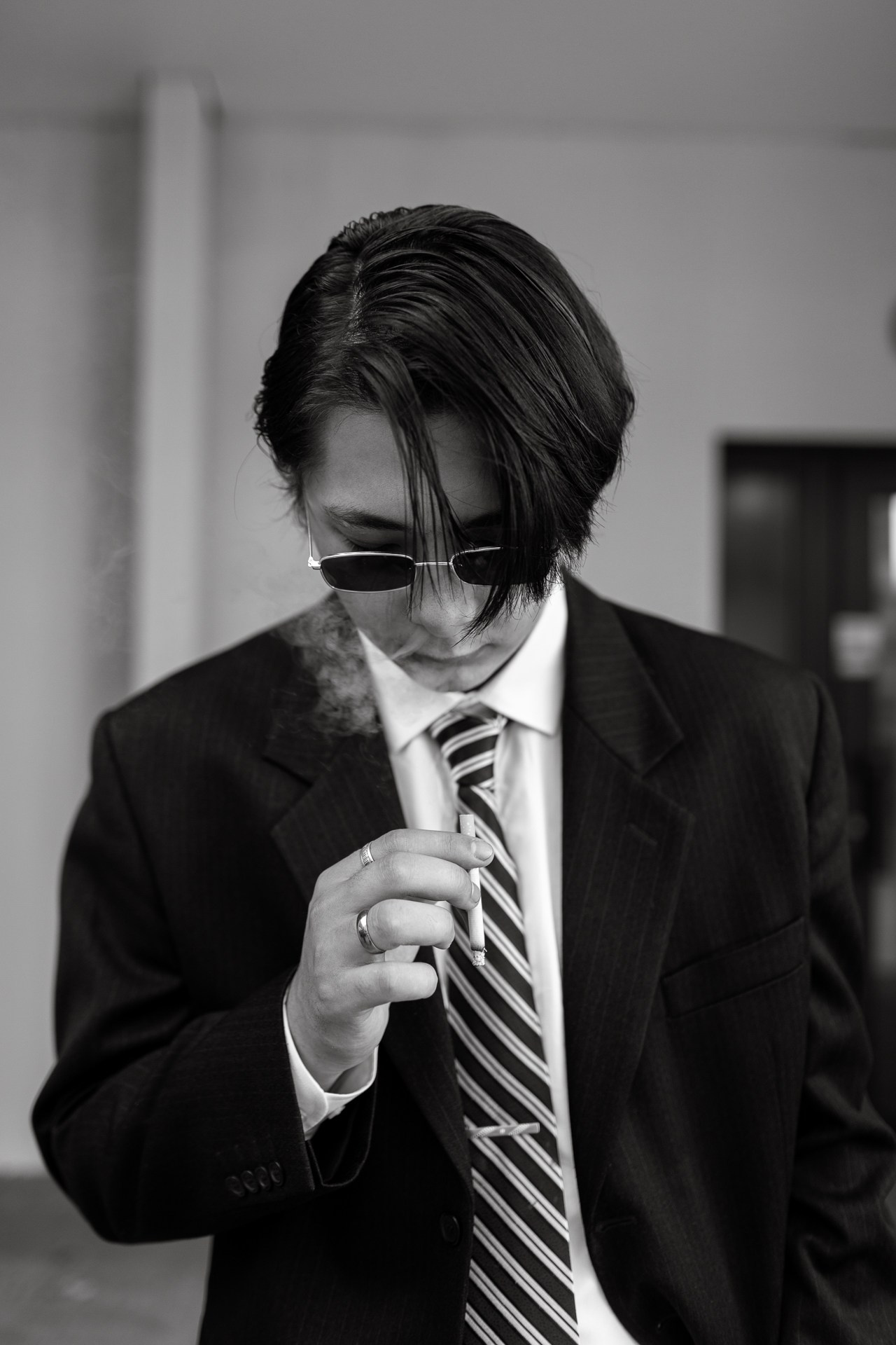 Мужчина красиво курит. Черное-белое фото азиата, который курит. Парень в костюме и очках.