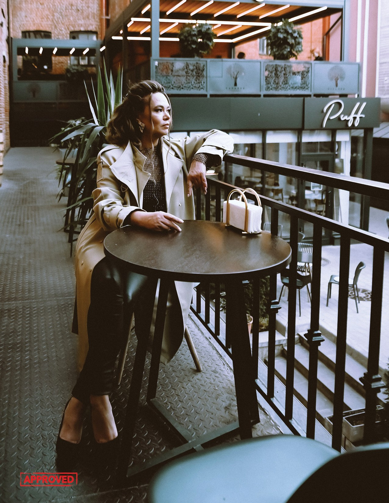 На фото девушка сидит за столом возле кафе.