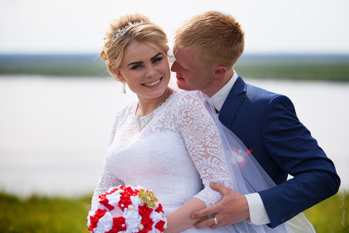 Счастливые Павел и Яна обнимаются на фоне бескрайнего поля и реки в день свадьбы