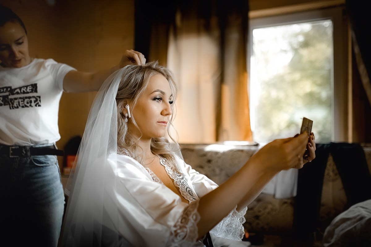 Сборы невесты. Невеста сидит в кресле смотрит в зеркалце во время макияжа в комнате в Санкт-Петербурге