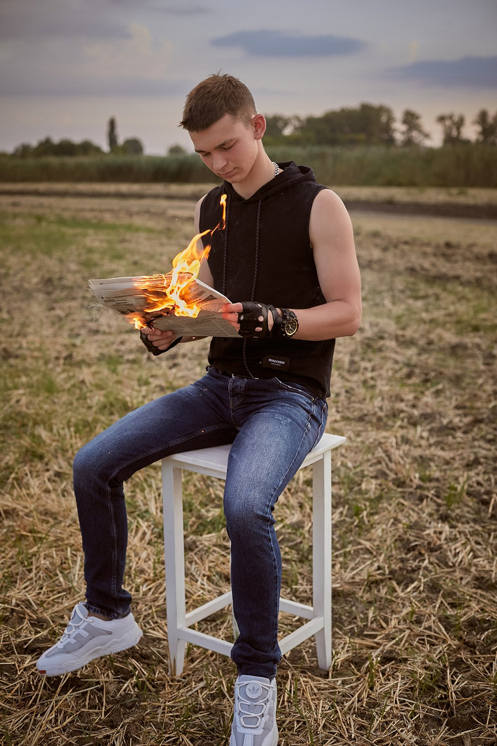 Фотограф в Москве. Креативное фото. Парень с горящей газетой сидит на стуле в поле на закате.
