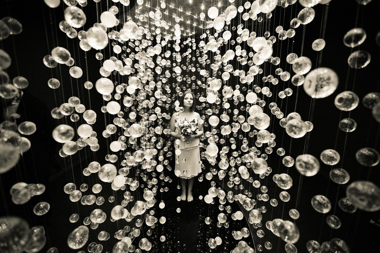 невеста с букетом в руках позирует на фоне сотни светящихся стеклянных шариков