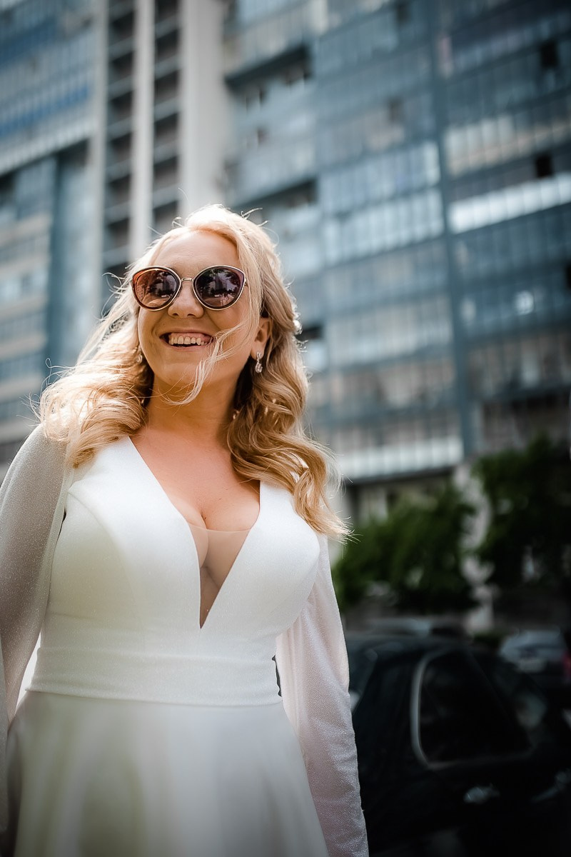 портрет невесты в солнцезащитных очках в движении на фоне ЗАГСа на Васильевском острове в Санкт-Петербурге. Вертикальный поясной кадр.