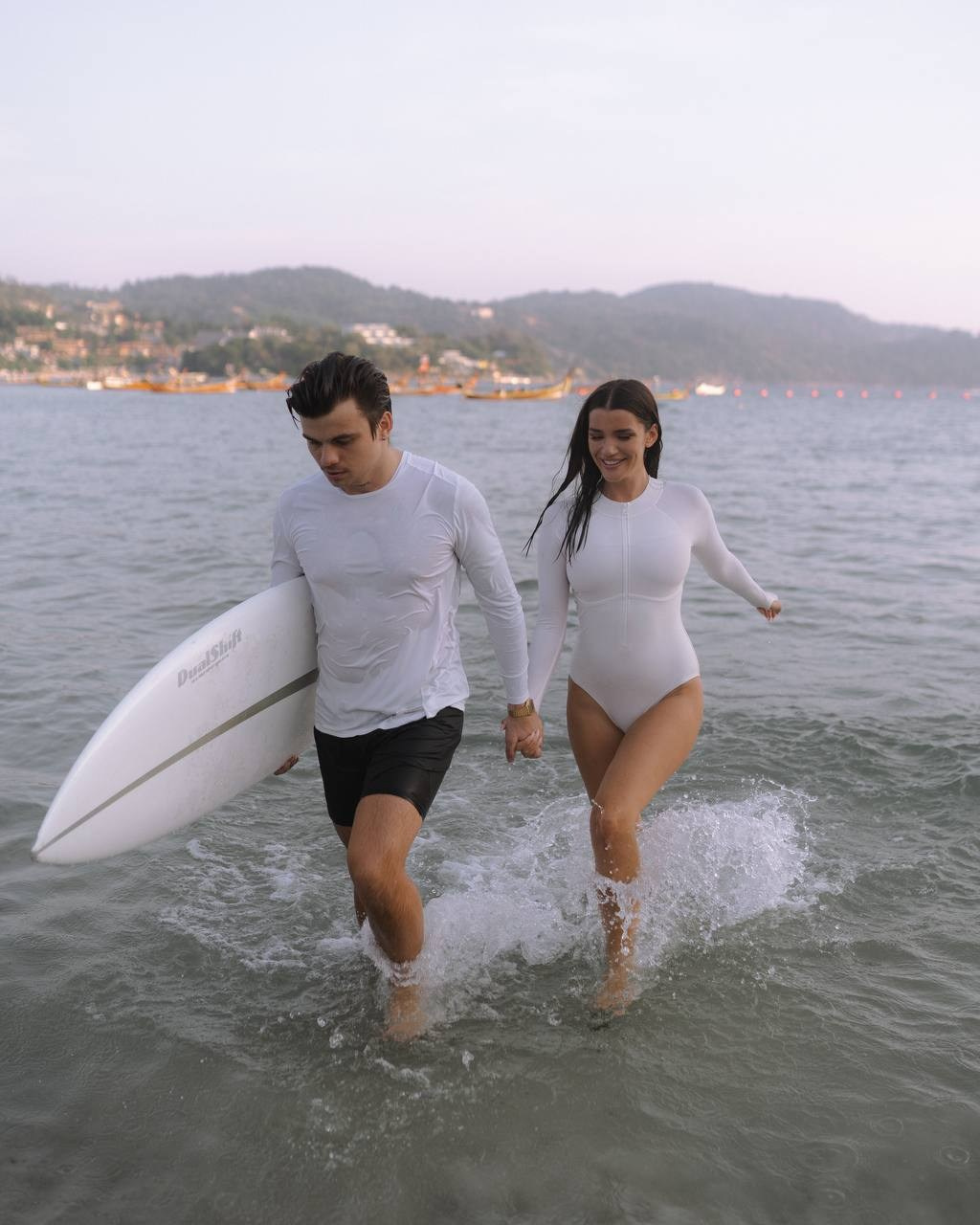 Пара выходит из воду с доской для сёрфинга — прогулка по берегу