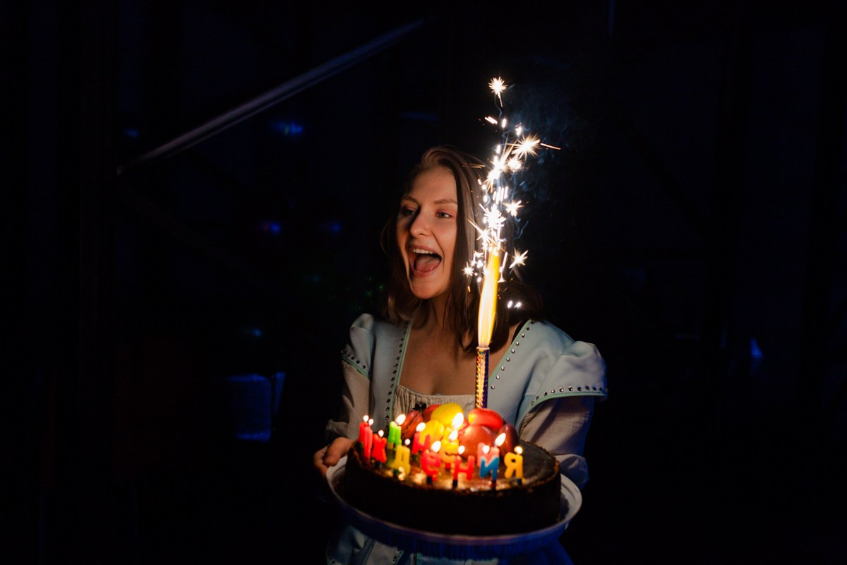 Девушка аниматор выносит праздничный торт с горящей свечой на детском день рождении