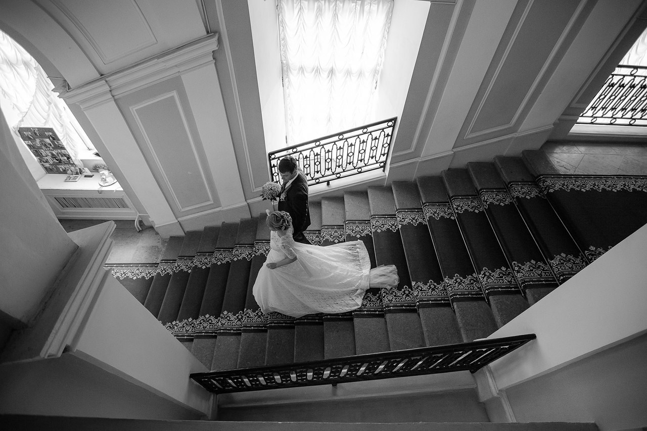 вид сверху на молодожен спускающихся по красной ковровой дорожке широкой мраморной лестницы