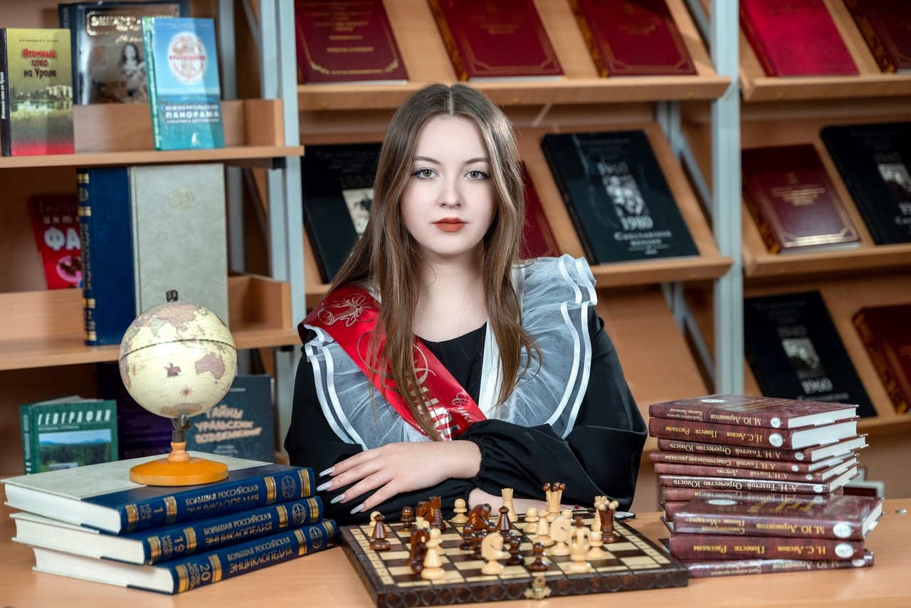 Девочка за партой в красивом фартуке с красной ленточкой выпускника.