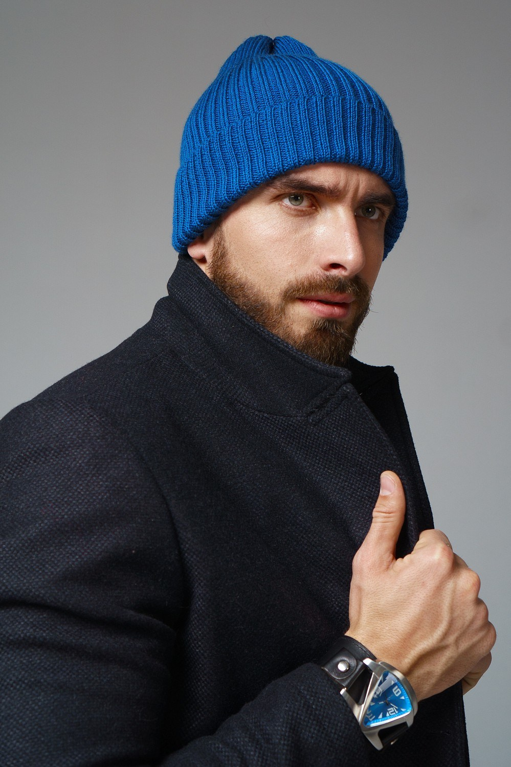 Мужчина с бородой в черном пальто и яркой синей шапке