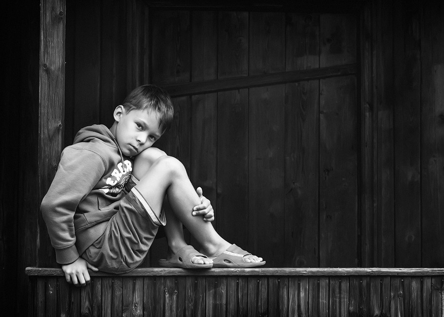 Мальчик сидит на деревянной перекладине . Портрет сидящего мальчика.