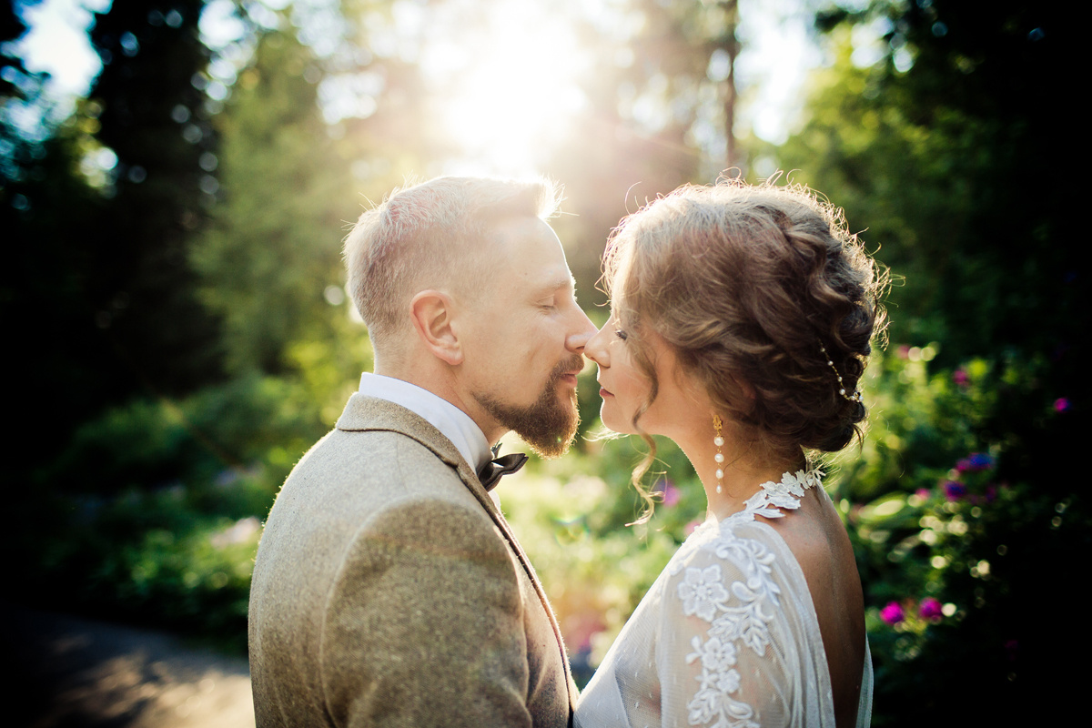 жених и невеста целуются в контровом свете на фоне зелени