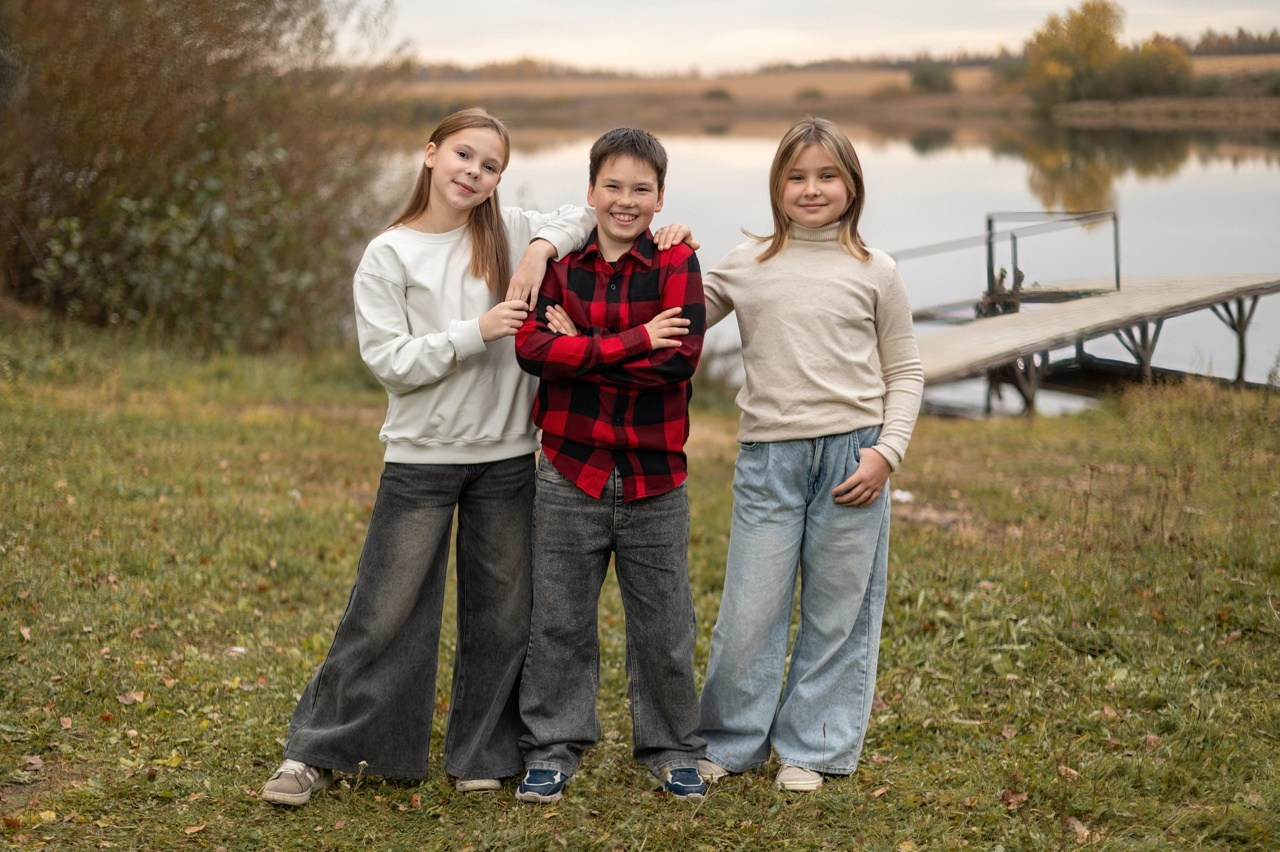 Одноклассники позируют фотографу стоя на зеленой траве осенью возле пантона.