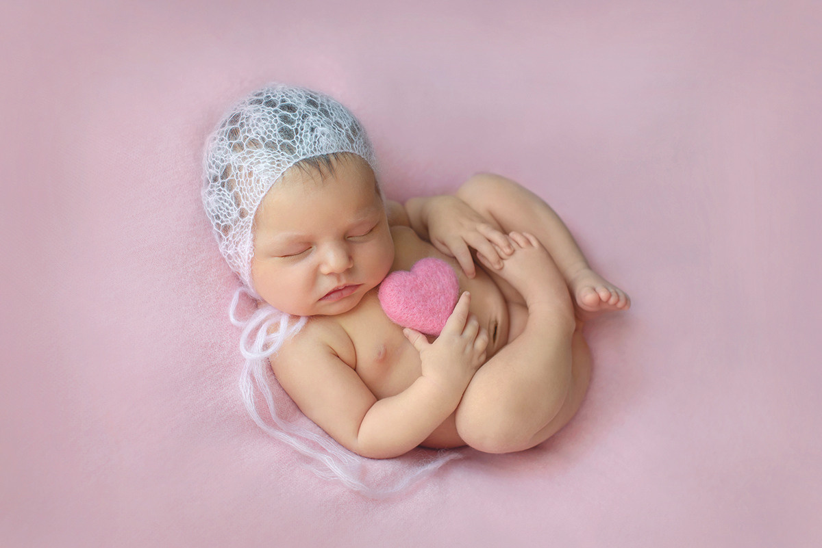 новорожденный лежит в позе на спинке держит игрущку сердечко