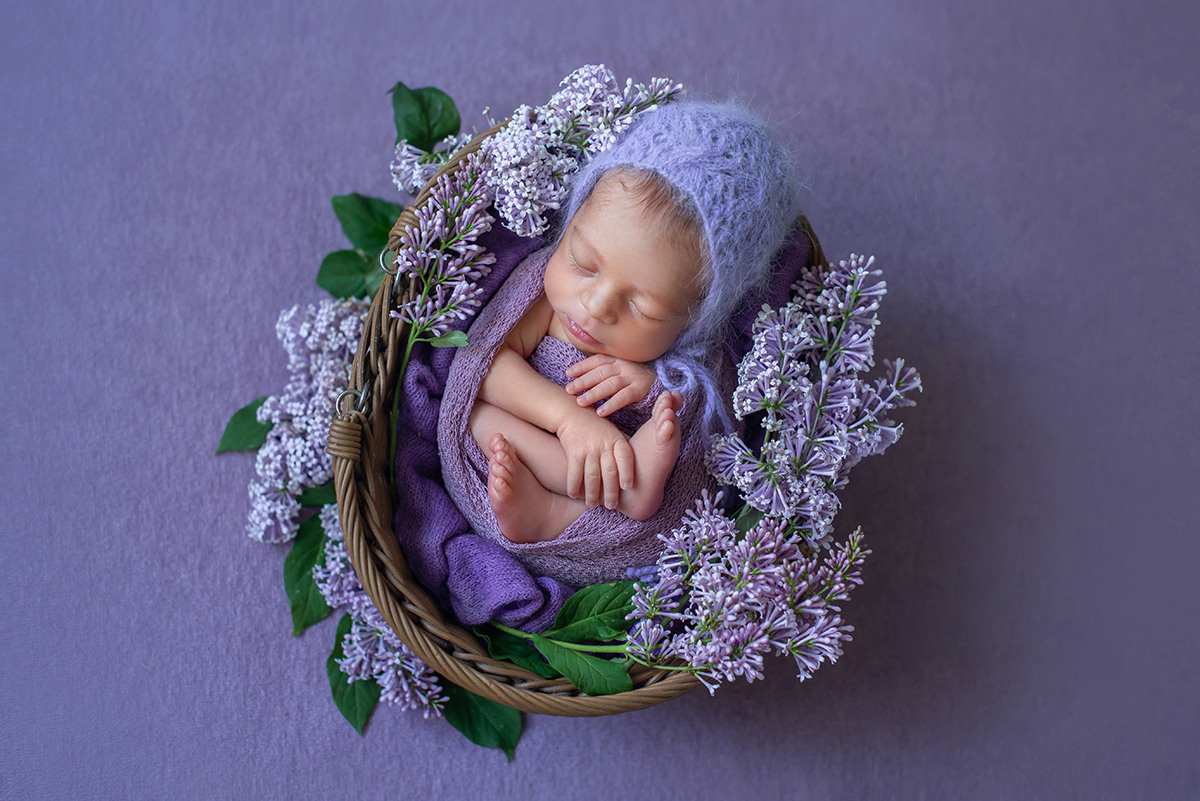 новорожденная девочка лежит в корзинке украшенной живыми цветами сирени