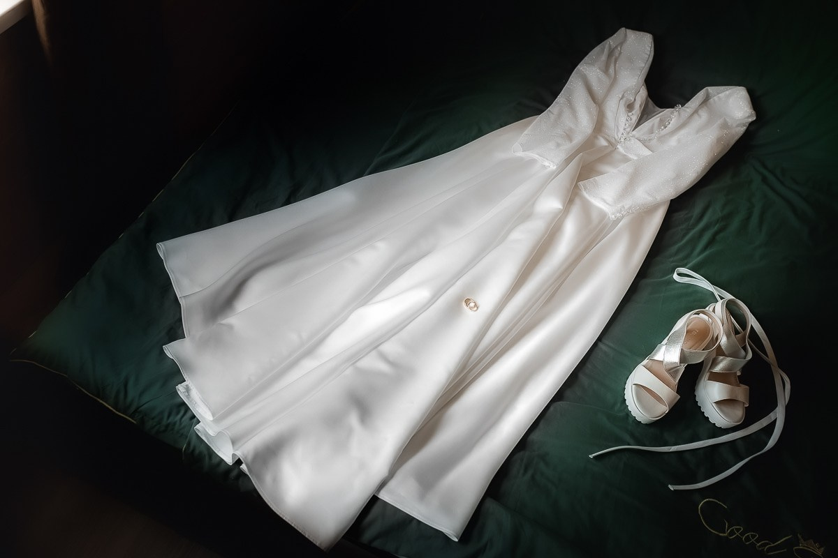 Свадебное белое платье и туфли невесты лежат на кровати  в комнате в Санкт-Петербурге