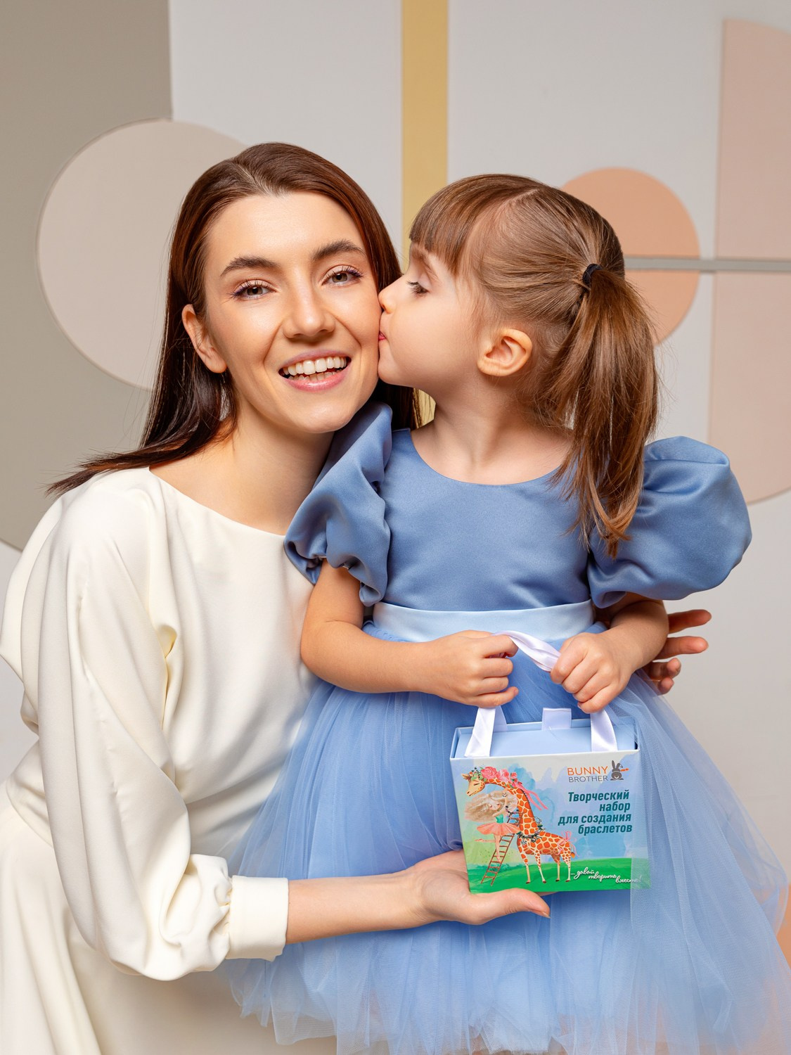 Дочь целует маму, в руках у них бумажная коробка.