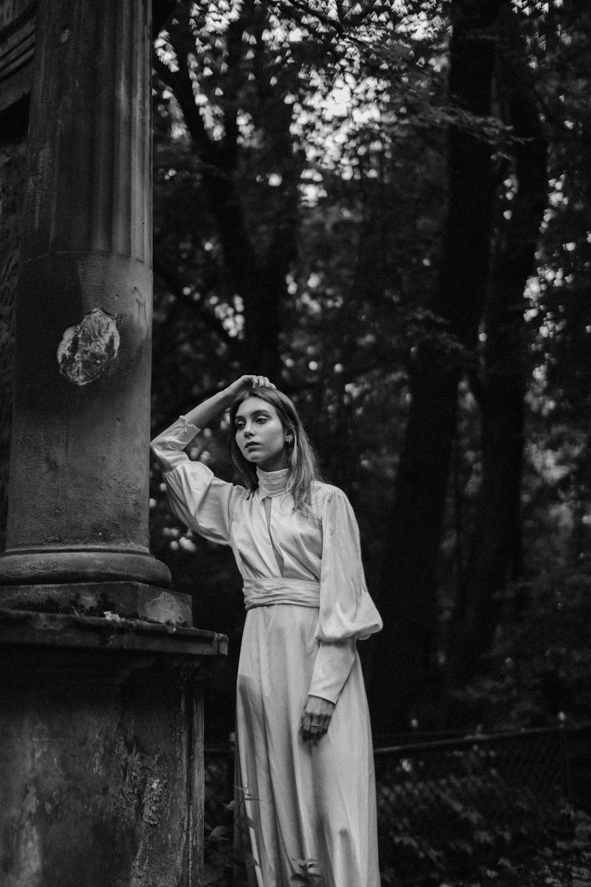 Девушка в белом платье прислонилась к каменной колонне
