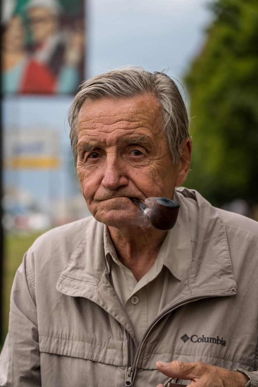 дедушка с глубокими морщинами в куртке курит трубку на улице