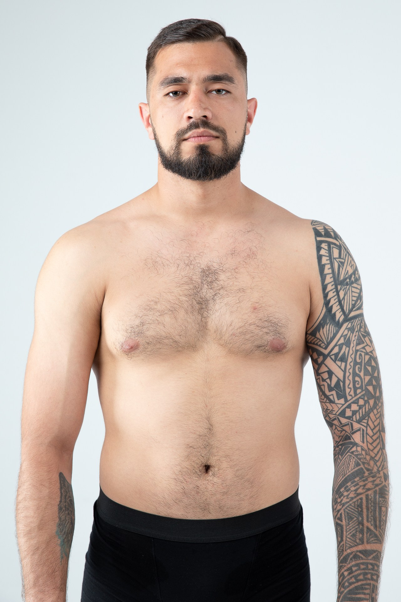 Мужчина модель с бородой с татуировками в черных трусах