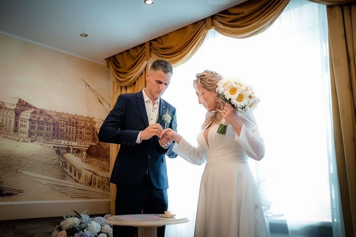 Жених надевает невесте кольцо во время регистрации брака в ЗАГСе на Васильевском острове в Санкт-Петербурге.  Горизонтальный поясной кадр.