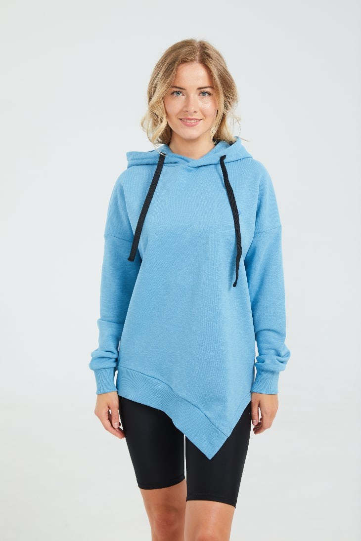 Девушка блондинка в голубом худи и черных леггинсах стоит на сером фоне