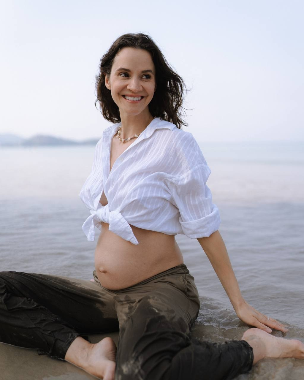 Девушка сидит у моря в белой рубашке