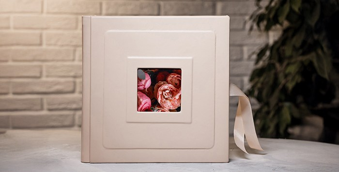 Фотокнига ручной работы в интерьере. Бежевая кожаная обложка с глубоким тиснением вокруг центрального фото с розовыми цветами и атласной лентой.