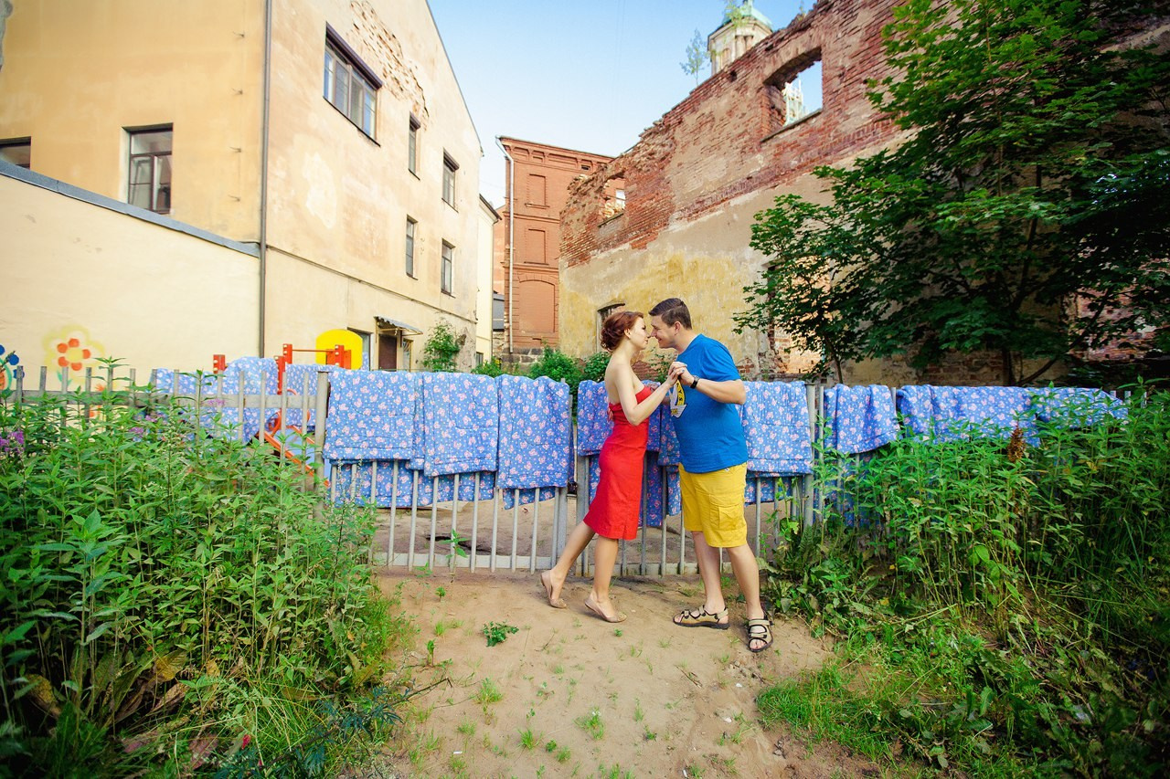 молодые мужчина и женщина целуются на фоне решетчетого забора на котором сушатся десять голубых одеял