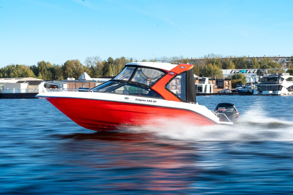 Красный катер Enigma на фоне берега, момент движения