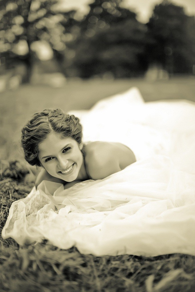 невеста в белоснежном платье улыбается, лежа на траве в парке