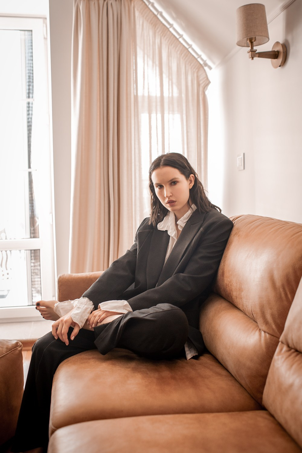 Девушка в пиджаке на коричневом диване в доме