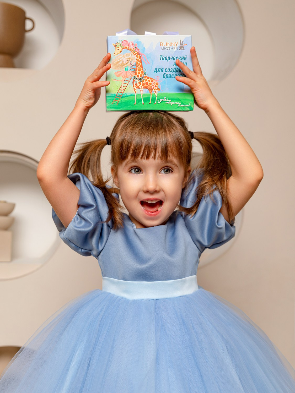 Девочка в голубом платье с коробкой в руках на сером фоне.
