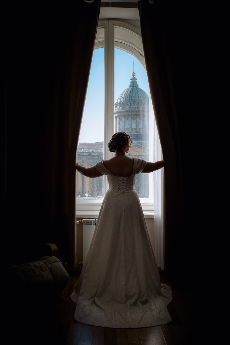 Невеста в отеле смотрит в окно на Казанский собор Петербурга