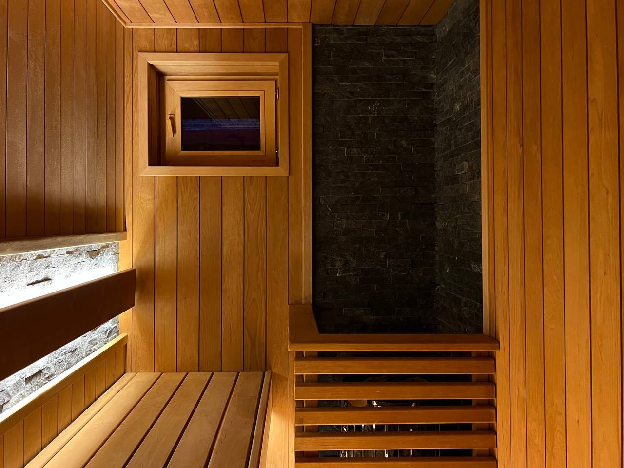 Семейная сауна в Охте: термоольха, природный камень и аккуратное реечное ограждение печи, защищающее любопытные детские ручки. SaunaTopMasters