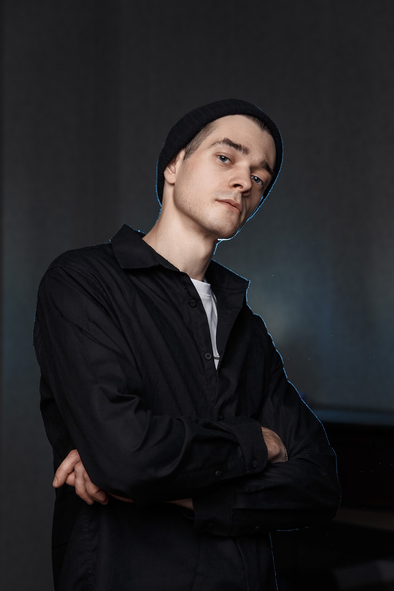 Парень в черной рубашке и шапке на темном фоне