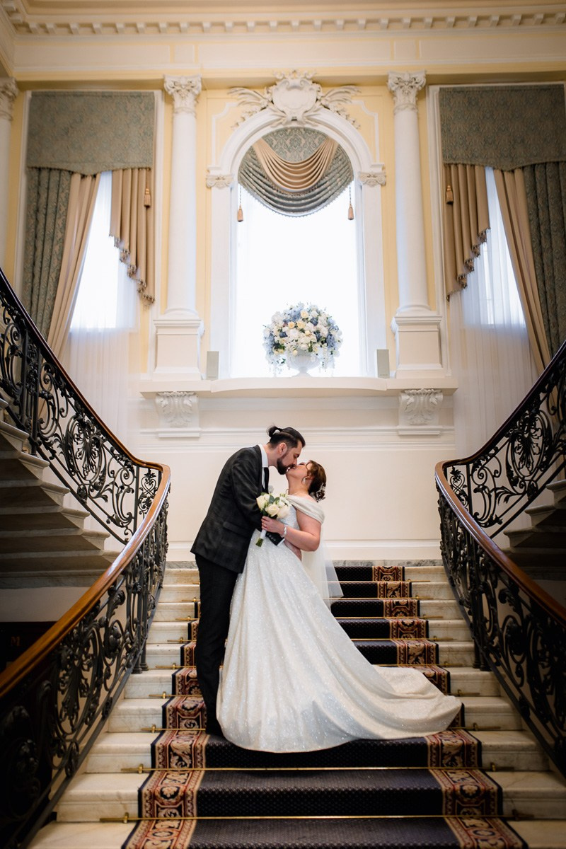 Жених и невеста целуются на лестнице в ЗАГСе на фурштатской СПб. Вертикальный кадр