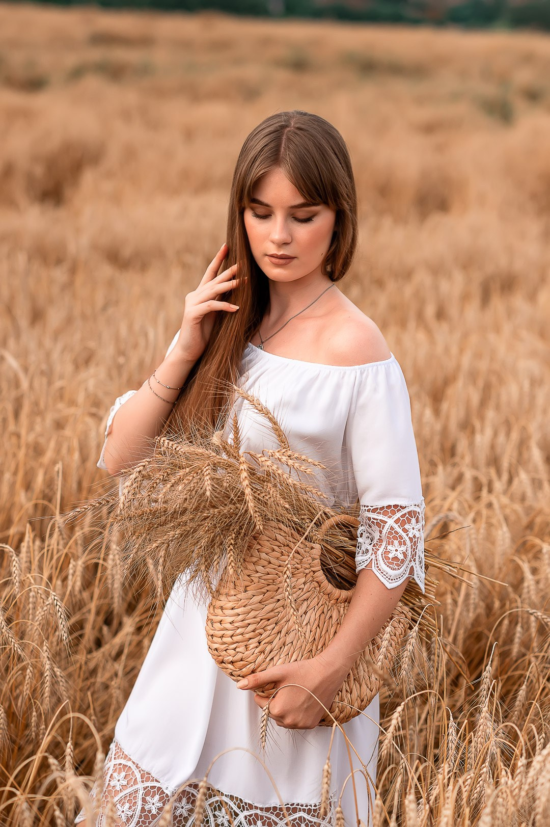 молодая красивая девушка держит в руках корзину с созревшими колосьями пшеницы
