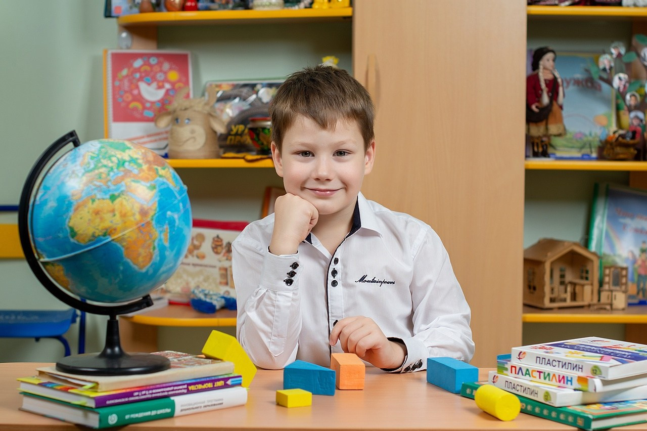 Мальчик позирует фотографу сидя на стульчике в детском саду.